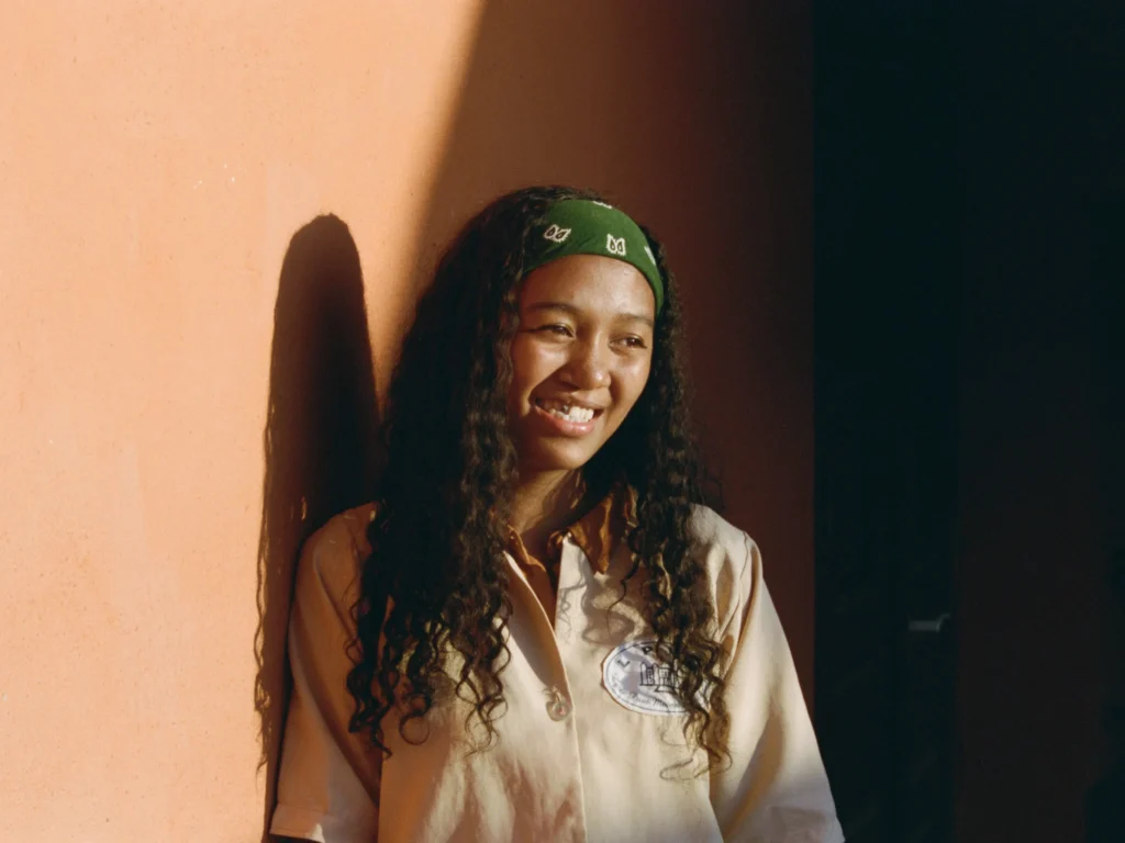 Narya leans against a wall, smiling for the camera.